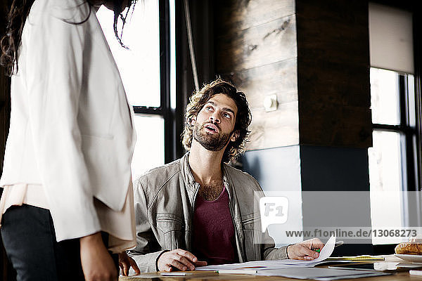 Mann schaut Geschäftsfrau an  während er im Büro sitzt