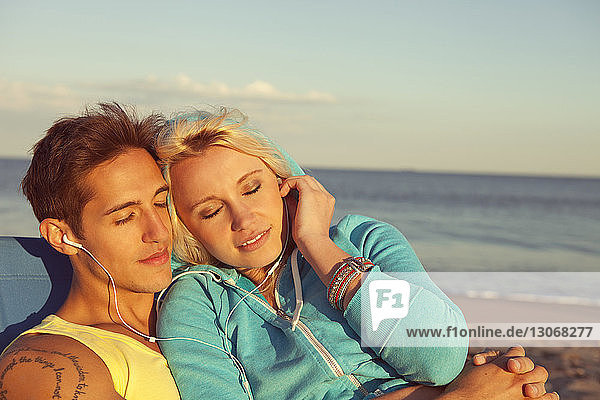 Couple relaxing while listening music on headphone at beach