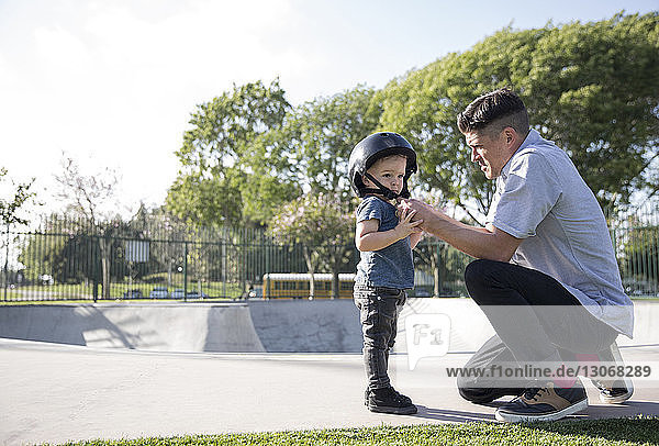 Seitenansicht des Vaters  der dem Sohn beim Helmtragen im Skateboard-Park hilft