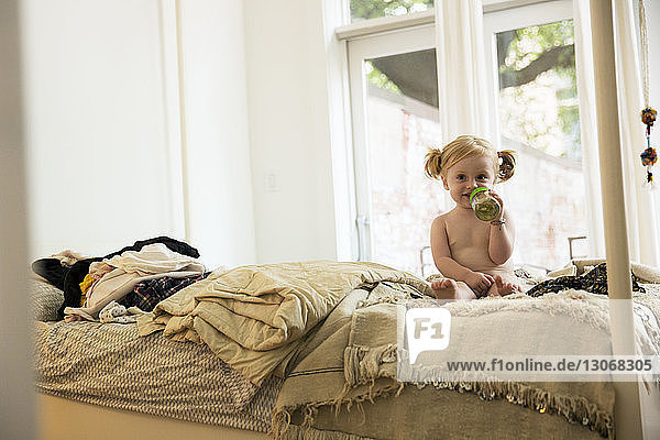 Porträt eines kleinen Mädchens  das zu Hause auf dem Bett sitzt und die Flasche hält