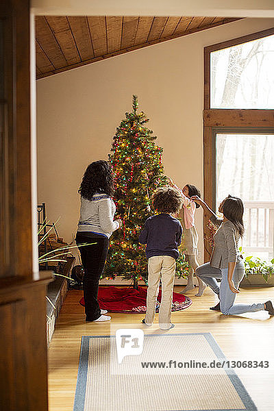 Familie schmückt zu Hause den Weihnachtsbaum am Fenster
