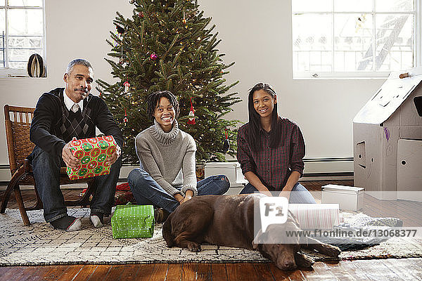 Glückliche Familie mit Hund sitzt zu Hause am Weihnachtsbaum
