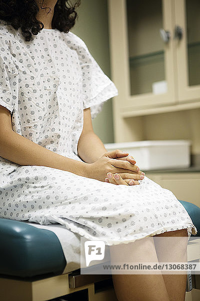 Mitschnitt einer Frau mit gefalteten Händen  die im Krankenhaus auf dem Bett sitzt
