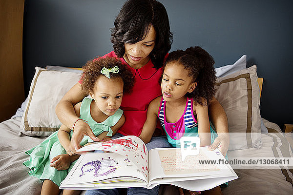 Mutter und Kinder schauen im Buch  während sie zu Hause auf dem Bett sitzen