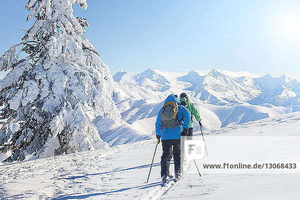 Rückansicht von Freunden mit Skistöcken beim Spaziergang auf schneebedecktem Feld