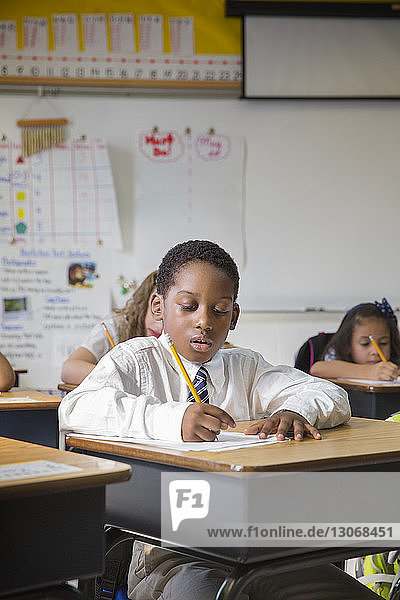 Boy writing on paper while sitting at desk in classroom