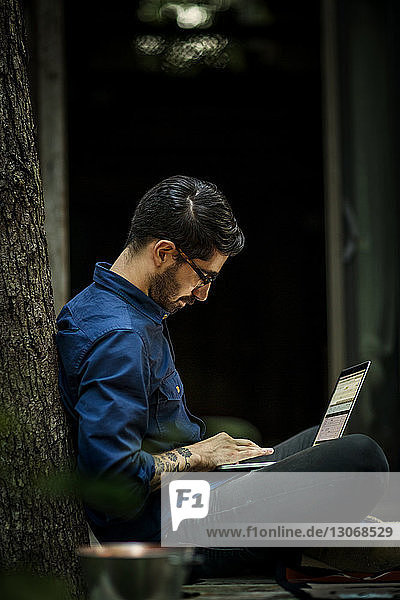 Mann benutzt Laptop-Computer  während er auf einem Baumhaus im Wald sitzt