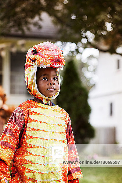 Cute boy wearing dinosaur costume standing in yard during Halloween