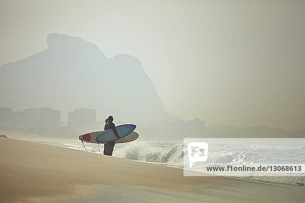 Paar  das Surfbretter trägt  während es am Strand steht