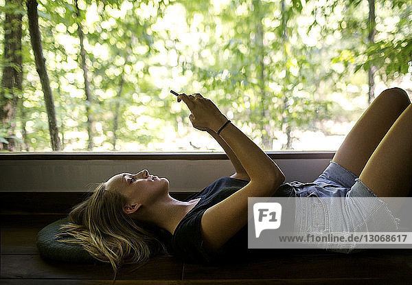 Frau benutzt Mobiltelefon  während sie zu Hause auf dem Fensterbrett liegt