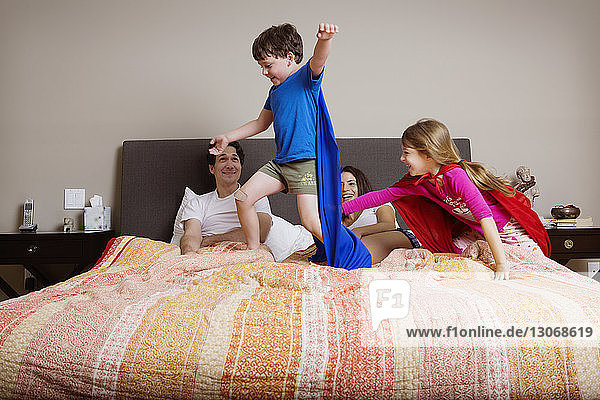 Playful kids in cape with parents on bed at home