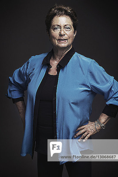 Porträt einer älteren Frau mit Händen auf der Hüfte vor schwarzem Hintergrund stehend