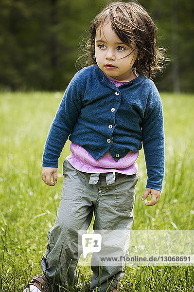 Girl looking away while standing on grassy field