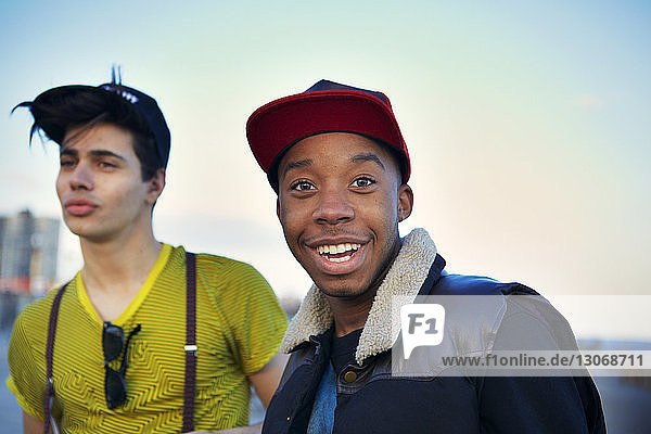 Portrait of smiling man with happy friend standing against clear sky