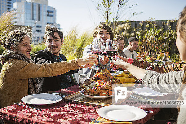 Friends toasting red wineglasses at outdoor table during garden party