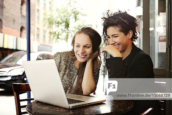 Freunde benutzen Laptop-Computer  während sie im Straßencafé sitzen