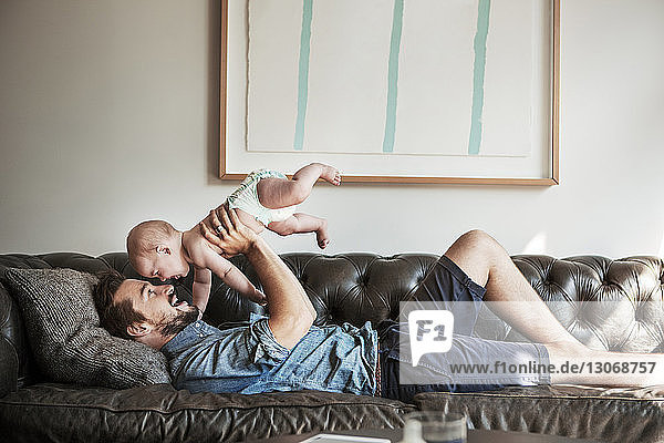 Side view of father lifting son while lying on sofa at home