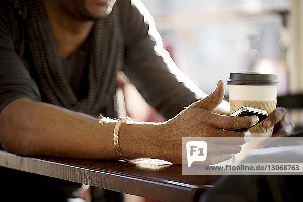 Mittelsektion eines Mannes  der ein Mobiltelefon benutzt  während er im Cafe sitzt