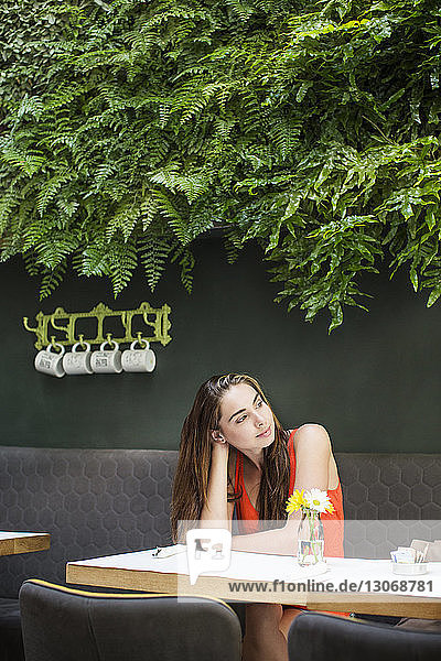 Nachdenkliche Frau sitzt am Tisch gegen Pflanzen im Cafe