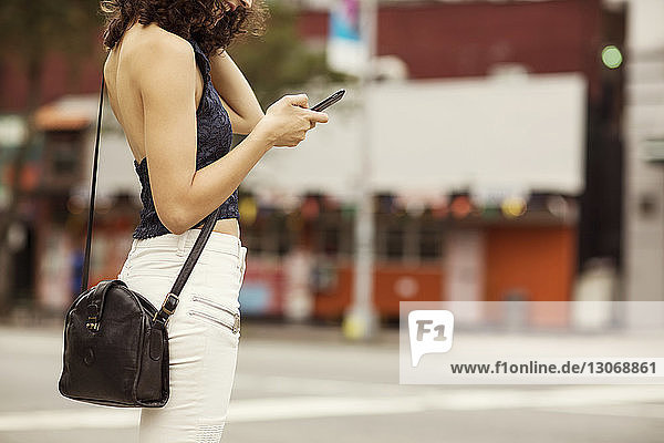 Ein Teil der Frau benutzt ein Smartphone  während sie in der Stadt auf der Straße steht
