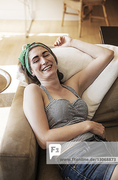 Hochwinkelansicht einer glücklichen Frau  die sich zu Hause auf dem Sofa entspannt