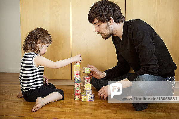 Vater und Tochter spielen mit Spielzeugblöcken  während sie zu Hause auf dem Boden sitzen