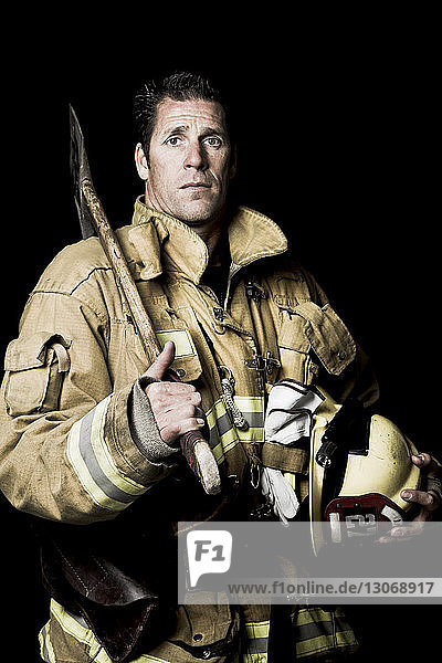 Porträt eines Feuerwehrmannes mit Schaufel vor schwarzem Hintergrund stehend