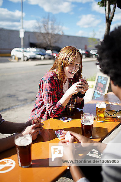 Glückliche Frau trinkt Bier  während sie mit Freunden am Tisch in einer Brauerei Karten spielt