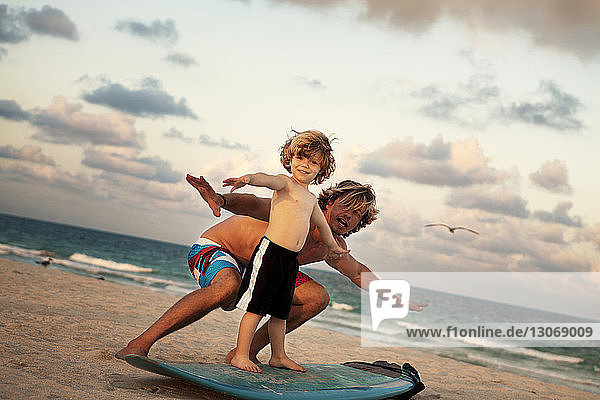 Porträt eines Vaters  der seinem Sohn das Surfen am Strand beibringt