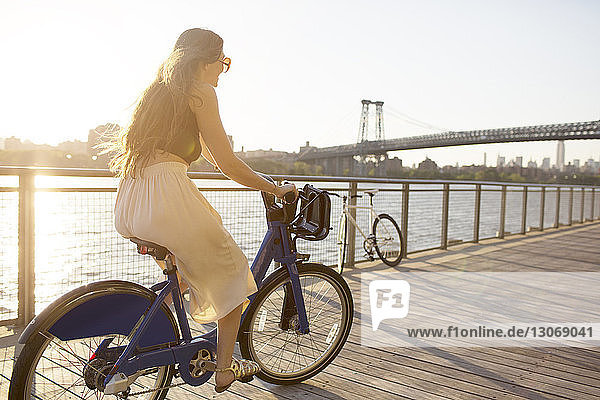Happy woman riding bicycle on promenade during sunset