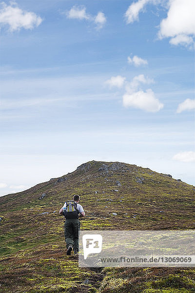 Rear view of man with backpack walking on mountain against sky