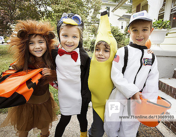 Fröhliche Kinder in Halloween-Kostümen  die während eines Streichs oder einer Behandlung zu Hause stehen