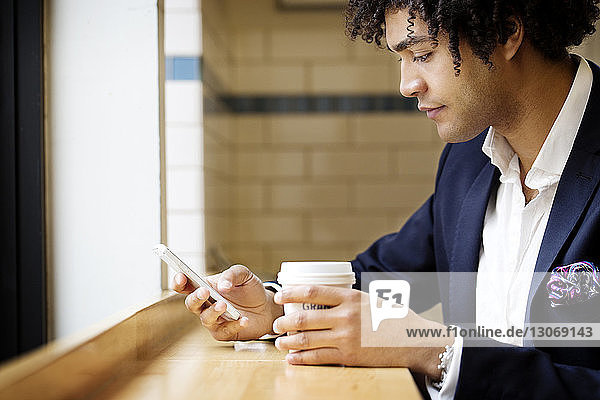 Side view of man using mobile phone while sitting at cafe