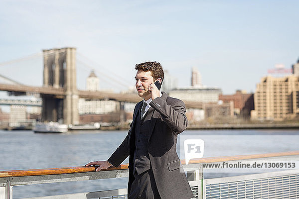 Businessman talking on smart phone while standing by railing against bridges