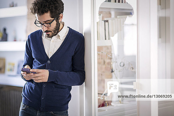 Man using mobile phone while leaning on wall at home