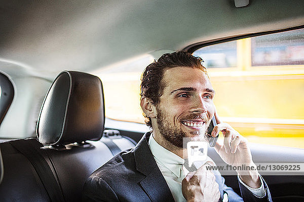 Lächelnder Geschäftsmann telefoniert während der Fahrt im Auto