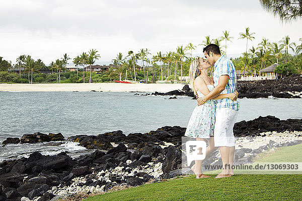 Couple kissing while standing on field against sea