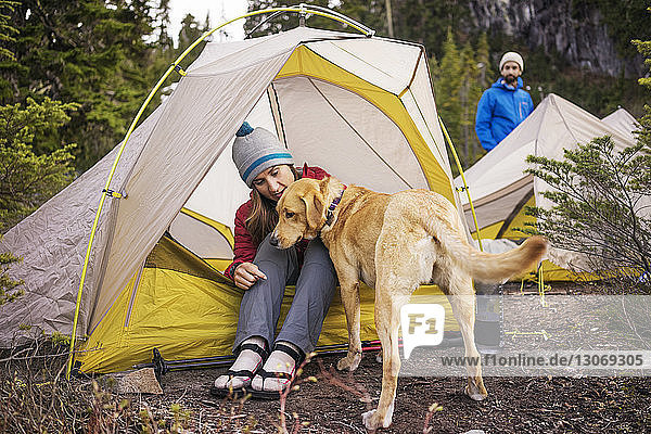 Frau mit Hund sitzt im Zelt  während der Mann am Feld steht