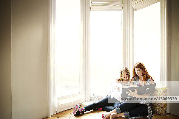 Mutter und Tochter lesen ein Buch  während sie zu Hause am Fenster sitzen