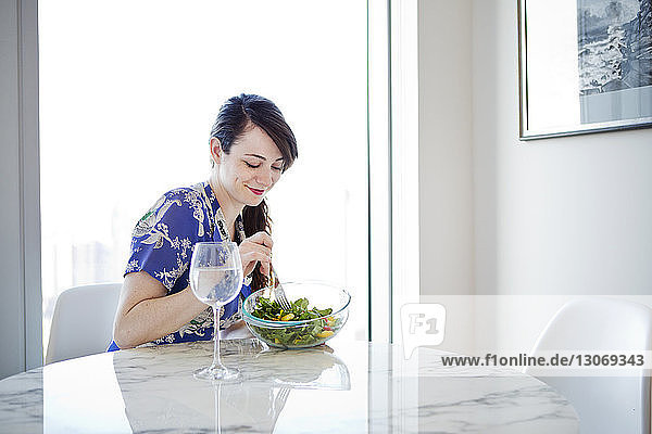 Frau isst Salat  während sie zu Hause am Tisch sitzt
