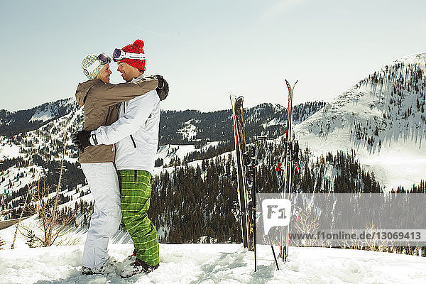 Side view of couple wearing ski-wear standing on snow covered mountain
