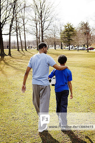 Rückansicht von Vater und Sohn beim Spaziergang auf dem Feld im Park
