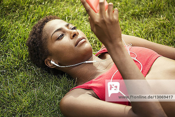 Hochwinkelaufnahme einer Frau  die ein Smartphone benutzt  während sie auf einem Grasfeld liegt