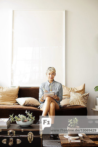 Porträt einer selbstbewussten Frau mit Buch  die zu Hause auf dem Sofa an der Wand sitzt