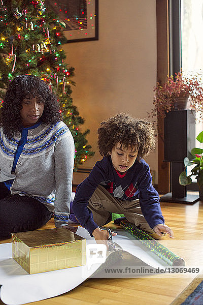 Mutter sieht Sohn an  der zu Weihnachten zu Hause Geschenkpapier schneidet