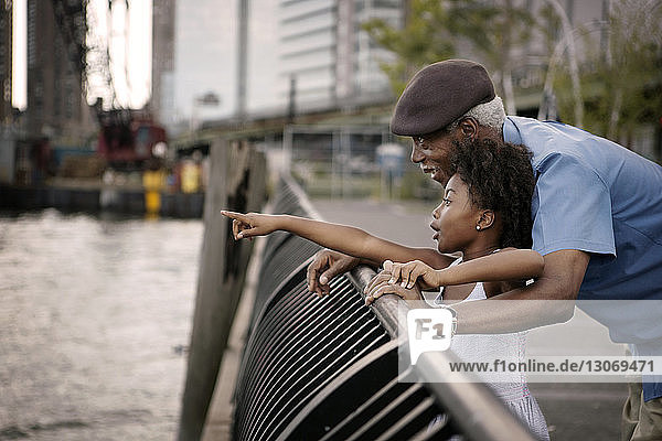 Aufgeregtes Mädchen zeigt Großvater beim Stehen am Geländer auf der Promenade in der Stadt