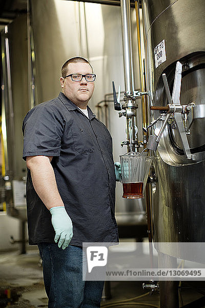 Portrait of worker removing beer from storage tank at distillery