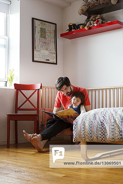 Father and daughter reading book while sitting at home