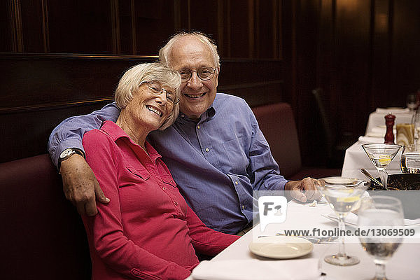 Porträt eines älteren Ehepaares mit Arm um den Arm im Restaurant sitzend