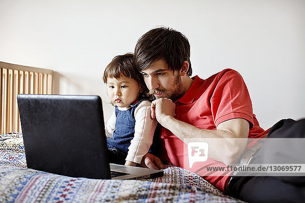 Vater und Tochter schauen auf Laptop-Computer  während sie sich im Bett entspannen